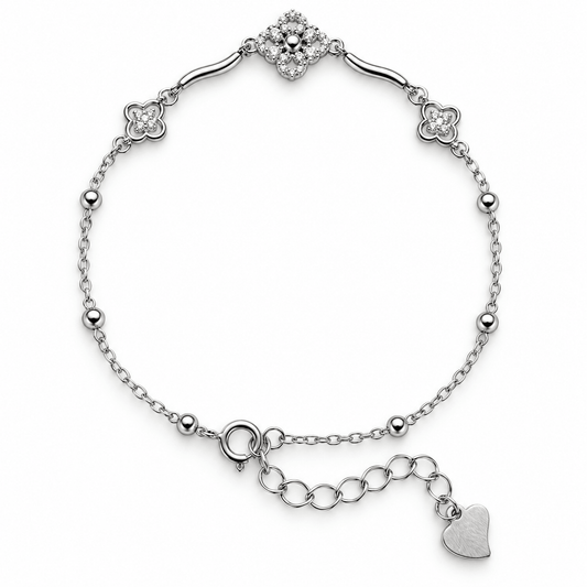 A silver chain bracelet with a floral cluster centerpiece, three clover motifs, small bead accents, and an extender chain featuring a heart charm, shown on a plain white background.